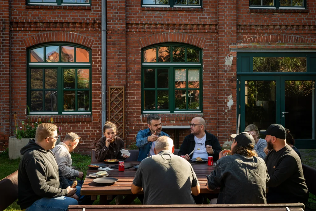 Community am Gartentisch vor der Backsteinfassade des HAVELWERK